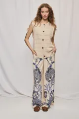 Chaleco de punto color beige, sin mangas, con escote redondo y cierre frontal con botones carey. Presenta diseño calado y silueta amplia.