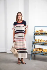 Vestido largo de tejido calado con rayas horizontales en tonos beige, marrón y amarillo. Tiene corte recto, hombros caídos, tajo lateral y logo bordado en la manga.