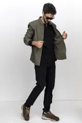 Camisa verde militar de corte recto, con cuello clásico, cierre frontal con botones a presión, mangas largas con puños abotonados, dos bolsillos de parche en el pecho y bajo redondeado.