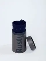 Boxer azul marino de la marca Rusty, presentado en un envase tubular cilíndrico con el logo de la marca impreso en grande.