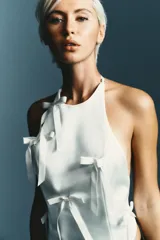 Top blanco de cuello halter y hombros descubiertos, con detalle de lazos en el delantero y cierre en la espalda con tira ajustable.