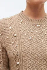 Sweater color beige melange de tejido de punto con diseño de trenzas y detalles de perlas en el frente y las mangas.