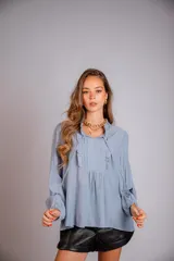 Camisa celeste con cuello con volados y lazos, mangas largas con puños elásticos y corte holgado.