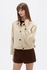 Chaqueta corta de algodón color beige, con cuello camisero, bolsillos laterales y cierre frontal con botones oscuros.