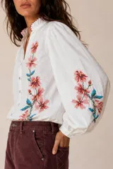 Camisa blanca de manga larga con bordados florales en tono rojo y verde en el frente y las mangas. Presenta cuello mao con escote en V y botones frontales.