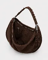 Bolso tipo hobo de gran tamaño, confeccionado en gamuza negra con detalles de costuras artesanales y tientos decorativos en los bordes. Cuenta con un asa trenzada con pespuntes a mano y cierre superior.