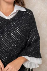 Poncho negro de tejido calado con destellos brillantes y terminación de flecos en el ruedo.