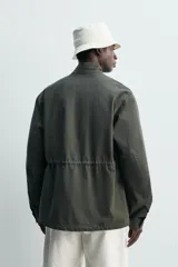 Cazadora regular fit de algodón color gris oscuro con efecto lavado, cuello subido, manga larga y cierre frontal con cremallera oculta por solapa con botones a presión. Cuenta con cuatro bolsillos frontales de plastrón con solapa y cintura ajustable con cordón interior.