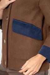 Campera de paño de lana color marrón con diseño oversize. Presenta cuello alto, cierre frontal con botones y detalles en pana azul marino en los puños y en las tapas de los bolsillos frontales.
