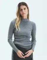 Polera de tejido de punto acanalado, color gris, con cuello alto y mangas largas. Presenta un ajuste al cuerpo y largo hasta la segunda cadera.