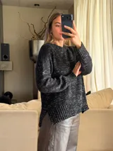 Sweater de punto con silueta holgada y cuello a la base, confeccionado en una mezcla de algodón y lurex que le otorga un acabado brillante. Presenta un diseño con aberturas laterales en el ruedo y puños acanalados.