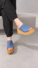 Zuecos con plataforma corrida de yute y suela de goma, capellada ancha de cuero sintético azul con textura croco y diseño abierto.