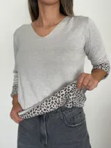 Sweater de punto color gris, con escote en V y manga larga. Presenta un diseño liso en el exterior y un interior forrado con estampado animal print que se revela en los puños al doblarlos.