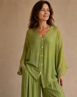 Camisa holgada de seda en color verde lima, con cuello en V, mangas largas amplias y cierre frontal de botones claros.