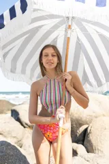 Trikini con diseño combinado, presentando un top de cuello halter con estampado de rayas verticales multicolores y una bombacha con estampado floral en tonos naranjas y rosas. La prenda cuenta con espalda descubierta y tiras ajustables.