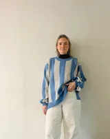 Sweater de punto con diseño de rayas verticales en tonos azul y gris, con sutil acabado brillante. Presenta cuello redondo, mangas largas con puños ajustados y corte amplio con aberturas laterales en el ruedo.