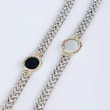 Pulsera de eslabones trenzados en plata con detalle central circular en oro que enmarca una piedra de ónix negra.