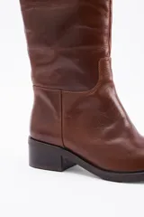 Bota de caña alta confeccionada en cuero vacuno, con taco cuadrado bajo y punta redondeada.