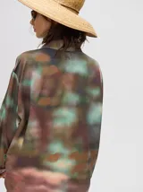 Camisa oversize de viscosa con estampado tipo tie-dye en tonos azulados. Presenta cuello clásico, cierre frontal con botones, bolsillo frontal con bordado y detalles de vivos en contraste en la tapeta y puños.