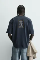 Camiseta relaxed fit color azul marino, con cuello redondo y manga corta. Presenta un estampado combinado a contraste en el delantero y la espalda. El estampado frontal es un texto en cursiva y un dibujo de tres figuras alargadas.