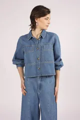 Camisa de denim celeste, de corte cropped, con cuello camisero, mangas 3/4 abullonadas y cierre frontal con botones.