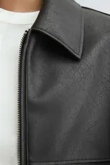 Cazadora de corte relajado confeccionada en tejido efecto piel, con cuello solapa, cierre frontal de cremallera y bolsillos de vivo en la parte frontal.