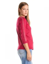 Buzo de tejido fino en color blanco, con cuello redondo y mangas tres cuartos tipo raglán. Presenta un detalle decorativo de tachas metálicas a lo largo de las mangas.