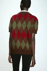 Chaqueta de punto de manga corta con cuello polo y cierre frontal de botones. Presenta un diseño estampado de rombos en tonos marrón, rojo y verde.