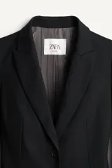 Blazer negro de corte recto de la colección Zara Studio, con solapas de muesca, cierre frontal de dos botones y bolsillos con solapa. Presenta mangas largas con pliegues estructurados en los hombros y forro interior a rayas a contraste.
