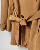 Campera tipo trench de color habano, de corte a la cadera, confeccionada en material textil símil gamuza. Presenta solapa cruzada, doble botonadura frontal, hombreras y cinturón ajustable para anudar en la cintura. Incluye bolsillos delanteros y puños con trabilla.