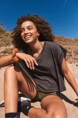 Camiseta deportiva de manga corta, color gris oscuro, con escote en V y diseño holgado. Presenta un detalle recortado en la espalda.