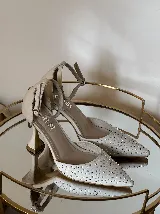 Zapato de tacón con punta fina, confeccionado en tela con aplicación de strass en la capellada y detalles en cuero en el talón, taco y pulsera. Cuenta con cierre de hebilla al tobillo y taco de altura media.