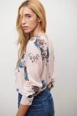 Camisa de manga larga con cuello redondo y cierre frontal de botones. Presenta un estampado floral en tonos azules y marrones sobre una base de color rosado claro.