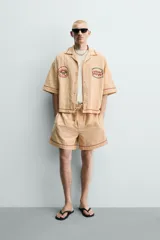 Shorts relaxed fit color beige con textura en relieve tipo jacquard, cintura elástica con cordón ajustable y detalle de bordado en contraste en el bajo.