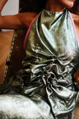 Top de fiesta color verde azulado iridiscente, con escote halter y frunces drapeados en el frente. Presenta un vivo de color naranja rojizo en el borde del escote y tiras para anudar en la espalda.