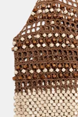 Top de crochet con escote recto y tirantes finos. Presenta un diseño bicolor con la parte superior en color marrón y la parte inferior decorada con abalorios en tonos crema y marrón.