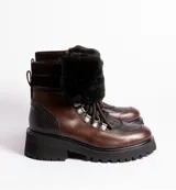 Borcegos de cuero vacuno en tonos marrón, con diseño de caña media y cuello con forro de piel sintética negra. Presentan cordones marrones, ganchos metálicos para ajuste y suela de goma tipo track con plataforma.