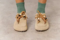 Zueco de cuero gamuzado color beige, con cordones decorativos con cuentas y piezas envueltas en cuero. Tiene plantilla acolchada y base liviana.