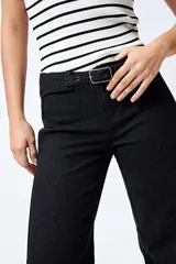 Jean negro de calce flare con cinturón incorporado en la misma tela y silueta ajustada en cadera que se ensancha hacia el ruedo.