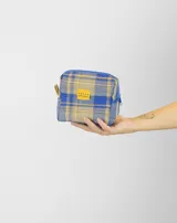 Neceser de viaje con diseño a cuadros en tonos azul y beige, confeccionado en tela de franela. Cuenta con cierre superior y etiqueta de marca en el frente.