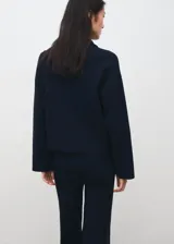 Jersey de punto color negro, con cuello polo y cierre frontal de cremallera, mangas largas y detalles de ribetes claros en las costuras.