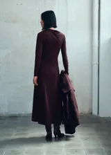 Vestido midi de corte evasé en color marrón oscuro, confeccionado en tejido elástico. Presenta cuello asimétrico, manga larga y diseño sin cierre.