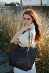 Bolso tipo tote de cuero con acabado envejecido en tonos oscuros. Presenta doble asa de hombro con detalle de tachas metálicas y nudos decorativos en la unión con el cuerpo del bolso. Cuenta con un diseño amplio y estructurado.