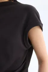 Top de punto fino color negro, con cuello elevado corto, mangas cortas con dobladillo y detalle de pliegues drapeados en un lateral de la cintura.