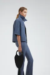 Sobre camisa azul de cuero ovino, corte boxy, mangas cortas, cuello clásico, botones a presión plateados y bolsillos delanteros.