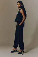 Pantalón tobillero negro de tejido arrugado, con cintura de tiro alto, pliegues delanteros y corte holgado de piernas barrel con elástico y cordón ajustable en los tobillos.