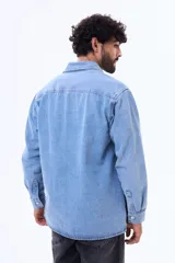 Camisa de jean de manga larga en tono azul claro, con cuello clásico, cierre frontal con botones y dos bolsillos delanteros con solapa.