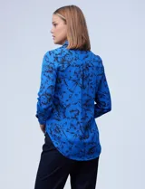 Camisa de gasa estampada con flores negras sobre fondo azul. Cuello con solapa y abertura central con botones.