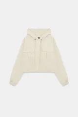 Cazadora color beige con capucha ajustable, manga larga con puño elástico, bolsillos frontales con solapa, bajo ajustable y cierre frontal con cremallera y botones a presión.