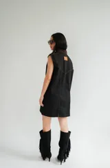 Vestido corto de jean color gris oscuro con efecto acid wash, sin mangas, con cuello camisero y cierre frontal de botones. Incluye dos bolsillos en el pecho con solapa y pespuntes decorativos.